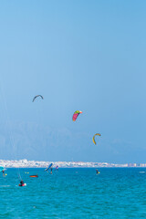 Kitesurfers and wingfoilers surfing and gliding across the Atlantic Ocean with the city of Tarifa and the mountains in the background.