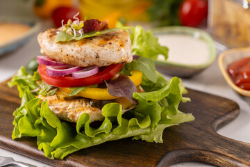 Poultry burger without a bun, served on a plate with bacon, vegetables and fries.