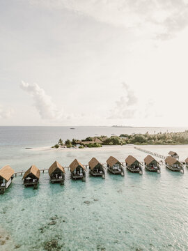 Aerial view of a luxury resort in the Maldives with overwater villas stretching into crystal-clear turquoise waters. The tropical paradise features white sandy beaches, lush greenery, and serene ocean
