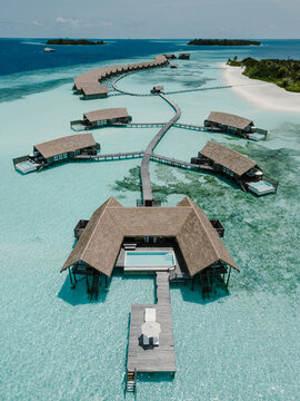 Aerial view of a luxury resort in the Maldives with overwater villas stretching into crystal-clear turquoise waters. The tropical paradise features white sandy beaches, lush greenery, and serene ocean