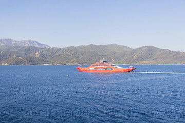 Obraz premium Ferry sailing through the clear blue sea waters of Greece, with mountains in the background. Summer vacation.