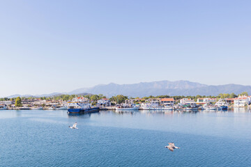 Breathtaking view of a picturesque Greek coastal town, with traditional houses, fishing boats, and a backdrop of mountains.