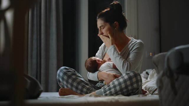 Authentic footage of a mother breastfeeding her newborn baby and drinking milk from the mother's breast. In the middle of the night the mother is tired and yawning. Concept of childhood and parenting 