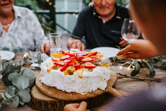 Woman cutting the pavlova cake topped with fresh fruits and berries
