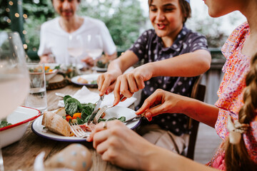 Young boy cutting food on her sisters plate.