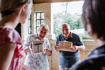 Senior couple bringing gifts greeted at the doorway by grandkids