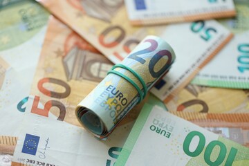 Roll of twenty euro currency bills lies on big amount of hundred and fifty euro banknotes