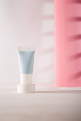Tender blue cosmetics tube on white concrete pedestal, pink paper roll on background. Blank label, unbranded template, mockup. Copy space. Product advertising banner