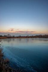 Beautiful blue hour on the lake, trees on the beach , sunrise over the lake with blue sky without clouds.Landscape photography on the pond , purple colors on the sky , trees and water , reflections 