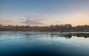 Fototapeta premium Blue hour on the lake , beautiful landscape photography on the lake with sunrise and reflactions on water , trees on the beach of the lake ,blue and orange colors.Blue sky . Water reflections 