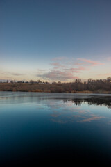 Fototapeta premium Blue hour on the lake , beautiful landscape photography on the lake with sunrise and reflactions on water , trees on the beach of the lake ,blue and orange colors.Blue sky . Water reflections 