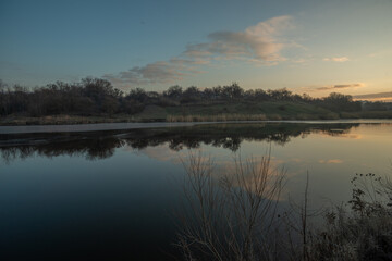 Obraz premium Beautiful sunrise on the pond , pond near the village .Red and orange sunrise in the sky , trees and houses , landscape on the lake with sunrise , reflactions on water 