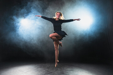 Contemporary woman dancer posing on black background with smoke. Adult female artist performer dancing with expression. Modern ballerina dancing in darkness. Passion dance in dark. Flexibility balance