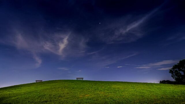 夜空を背景にした公園の芝生の丘の上のベンチ（タイムラプス）