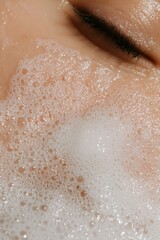 Fototapeta premium Woman's eye and face covered in foamy cleanser during skincare routine in soft light