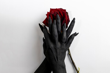 The black hands with long nails hold a rose and make it dry. Concept photo with woman hands painted in black paint with hold a red flower. 
