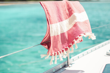 Red turkish towel hanging on wire railing of boat on the water