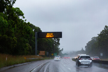 Cars traveling on slippery road with digital sign warning of hazardous driving conditions