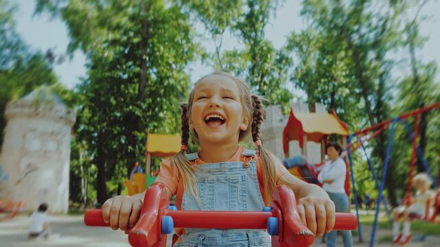 Cute little 4-5 year girl laugh and have fun, swinging on balancing swing in park. Pretty child rides on seesaw board, playing playground, happy childhood, positive real emotions. POV 