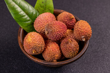 Fresh lychees with leaves resting in wooden bowl on dark background