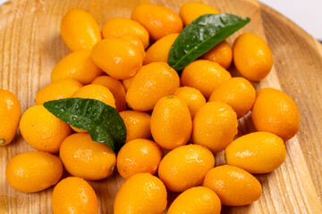 Fresh kumquats with leaves resting on wooden plate