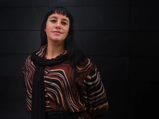 A confident woman in a stylish brown patterned blouse poses playfully against a sleek dark background, showcasing modern fashion and natural charm in an urban setting © Jesus-Salas-Dual