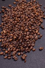 Roasted coffee beans scattered on dark background forming a pile