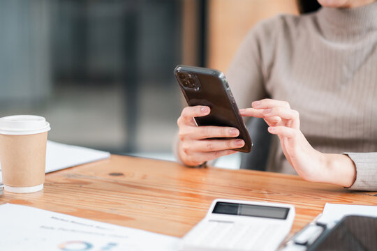 Professional woman using smartphone at office desk with coffee and calculator, focusing on productivity and technology. - Powered by Adobe