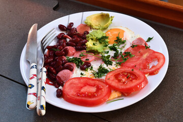 Full breakfast plate with baked beans, tomatoes, eggs, sausage and avocado in street cafe. Selective focus
