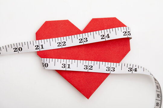 Measuring tape wrapped around red origami heart on white background