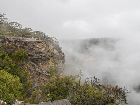 Hiker standing on observation point on top of mountain covered with clouds