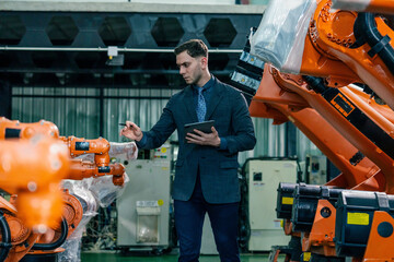Industrial engineer inspects robotic arms in modern factory during daytime