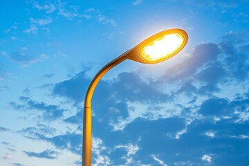 Against a serene blue sky with white, puffy clouds, a glowing LED lamp shines brightly, symbolizing efficient electric lighting