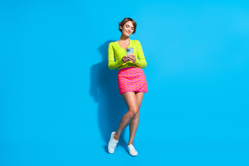 Full length body photo of young lady browsing social media using smartphone texting date boyfriend isolated on blue color background