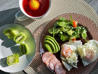 tasty healthy morning breakfast with a cup of coffee or tea. lots of food on the table with a green salad before starting the day. eggs with avocado and kiwi fruits. organic nutrition for health