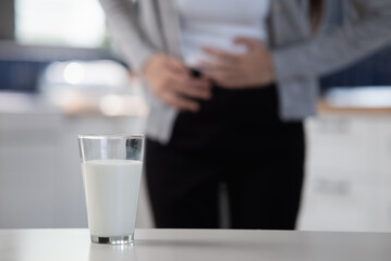 Allergy dairy food lactose intolerance allergen health care illness concept. Close up a glass of milk with blurred Asian woman holding stomach belly feel pain digestive unhappy after drink a cow milk.