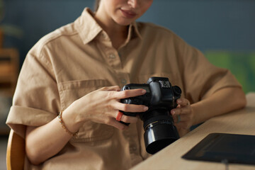 Woman focused on adjusting camera settings, sitting at desk with professional photographic equipment. Concentration evident in surroundings