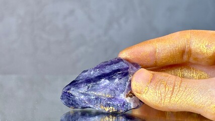 Close-up purple amethyst crystal in hand on grey abstract background. Mystical atmosphere....