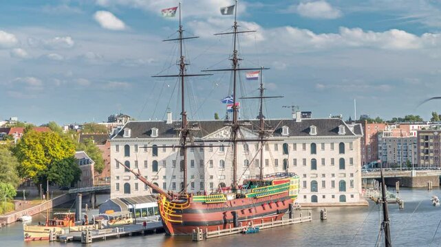 Aerial timelapse of the National Maritime Museum with the sailboat replica Amsterdam docked nearby. Blue sky with clouds. Famous for cultural activity, canals and bridges. Amsterdam, Netherlands