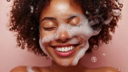 Fototapeta premium Close-up of a smiling woman with curly hair covered in soap bubbles, showcasing freshness and happiness, symbolizing skincare, beauty, and personal care in a joyful moment.