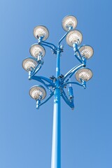 During the day, a sports stadium's light tower is silhouetted against a bright blue sky