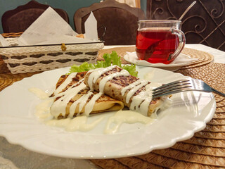 Delicious breakfast: pancakes with sour cream, a cup of tea on the table