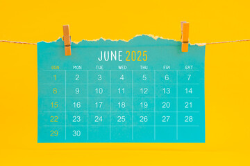 June 2025 calendar tearing hanged with brown rope on yellow background.