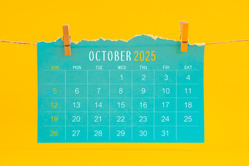 October 2025 calendar tearing hanged with brown rope on yellow background.