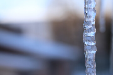 Icicles in the city close-up. Icicles against the background of blurred buildings. Long icicle with selective focus. Winter. Frosty weather. Frozen water in winter, close-up
