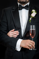 Groom in tuxedo holding champagne with woman's arm around him.