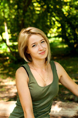 Blonde girl in a green T-shirt and jeans sits on a log in the park