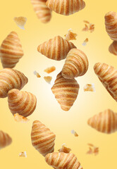 Delicious croissants and crumbs in air on golden background. Puff pastry