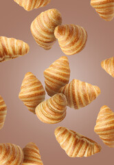 Delicious croissants in air on pale brown background. Puff pastry