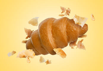 Delicious croissant and crumbs in air on golden background. Puff pastry